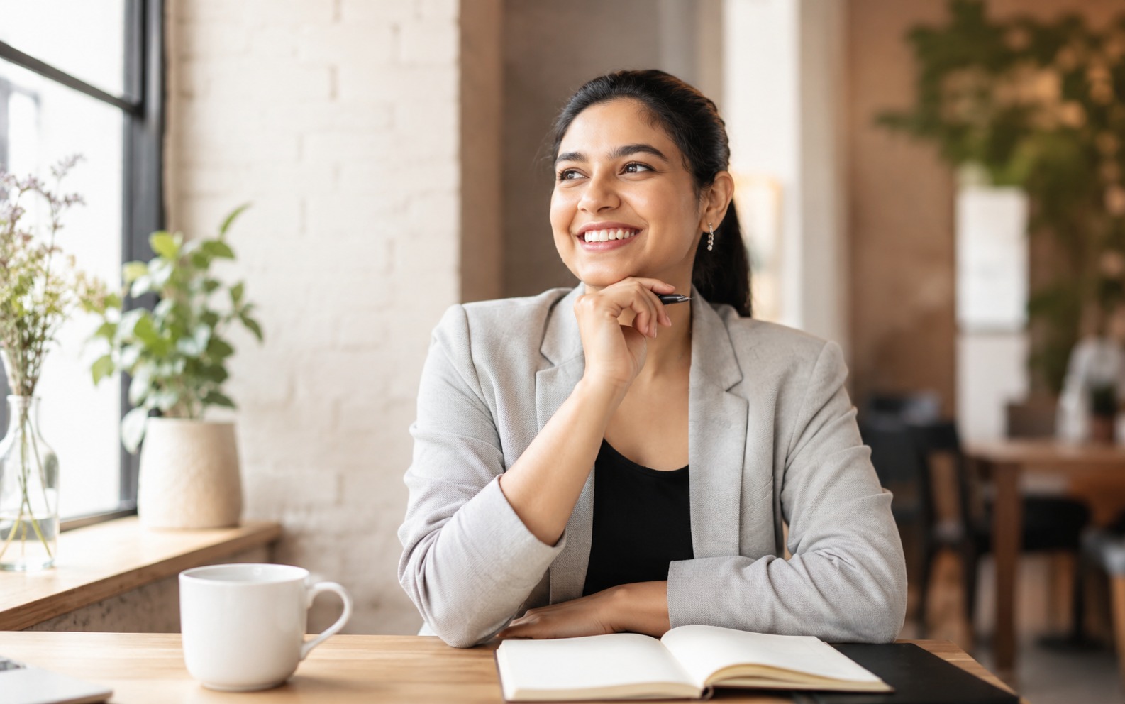 A young professional woman in a bright cafe workspace looking hopeful and energised